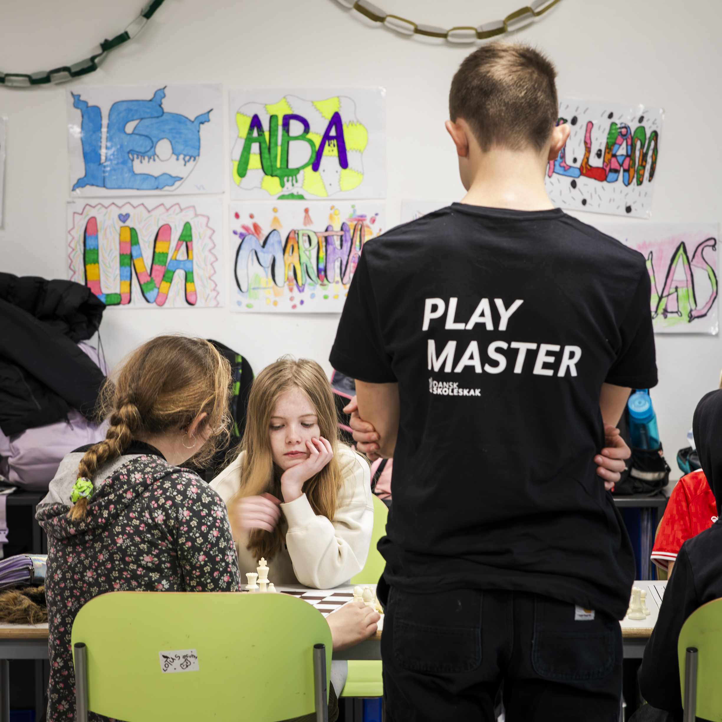 play master watching over a chess game between two other students